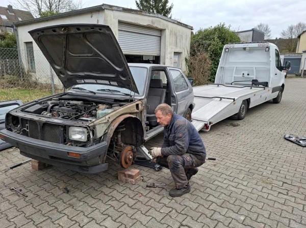 Teilweise ausgeschlachtetes Schrottauto mit fehlendem Rad wird für die Abholung vorbereitet