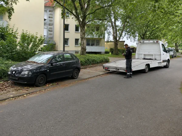Autoentsorgung Wetter: Abgemeldetes Schrottauto wird an einer Wohnstraße für die Abholung mit dem Autotransporter vorbereitet