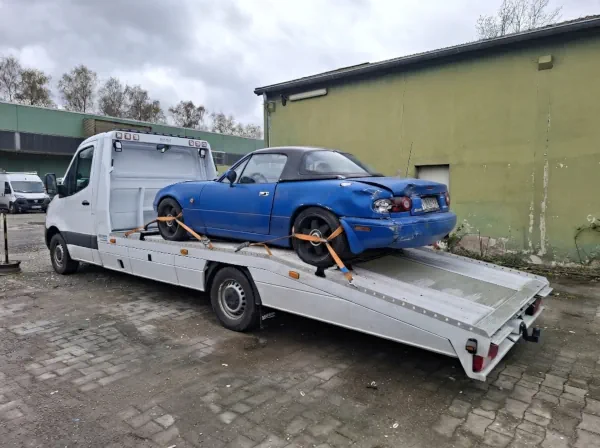 Älteres Fahrzeug mit sichtbarem Heckschaden wird auf einem Autotransporter zur endgültigen Verwertung abtransportiert