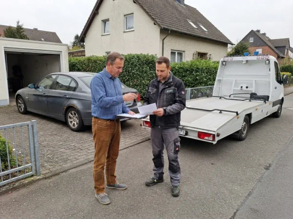 Bevollmächtigte Person übergibt Fahrzeugpapiere und Schlüssel für die Abholung eines älteren Wagens zur Autoverwertung